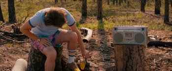 Movie still from “Prince Avalanche” (2013), directed by David Gordon Green – A man kneeling down in the dirt next to an old radio; Medium shot, Over the shoulder angle