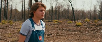 Movie still from “Prince Avalanche” (2013), directed by David Gordon Green – A man in overalls standing in the woods; Medium shot, Over the shoulder angle