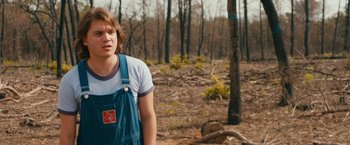 Movie still from “Prince Avalanche” (2013), directed by David Gordon Green – A man in overalls standing in the middle of a forest; Medium shot, Over the shoulder angle