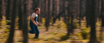 Movie still from “Prince Avalanche” (2013), directed by David Gordon Green – A man running through the woods holding a remote control; Wide shot, Over the shoulder angle
