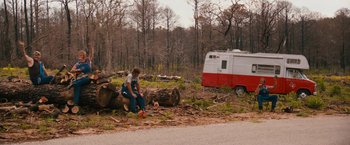 Movie still from “Prince Avalanche” (2013), directed by David Gordon Green – A woman sitting on a tree stump next to a camper van; Wide shot, Low angle