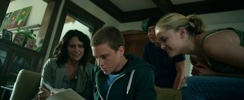 Movie still from “Project Almanac” (2015), directed by Dean Israelite – A group of people sitting around a table looking at a book; Medium shot, Low angle