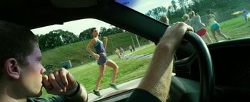 Movie still from “Project Almanac” (2015), directed by Dean Israelite – A woman is running in a field while a man is driving; Medium shot, Over the shoulder angle