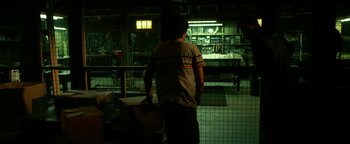 Movie still from “Project Almanac” (2015), directed by Dean Israelite – A man standing next to a cage in a dark room; Wide shot, Over the shoulder angle