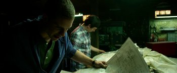 Movie still from “Project Almanac” (2015), directed by Dean Israelite – Two men looking at a map in a room; Medium shot, Low angle