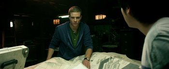 Movie still from “Project Almanac” (2015), directed by Dean Israelite – A man standing next to a pile of papers; Medium shot, Low angle