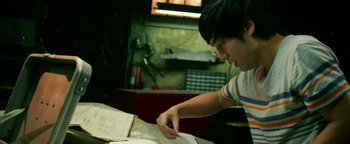 Movie still from “Project Almanac” (2015), directed by Dean Israelite – A young man looking at a book on a table; Medium shot, Low angle