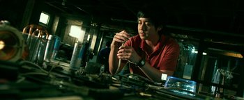 Movie still from “Project Almanac” (2015), directed by Dean Israelite – A man sitting in front of a table with many things; Medium shot, Low angle