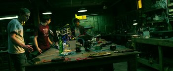 Movie still from “Project Almanac” (2015), directed by Dean Israelite – A man sitting in front of a table with a lot of electronics on top of it; Wide shot, High angle