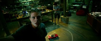 Movie still from “Project Almanac” (2015), directed by Dean Israelite – A young man standing in front of a red toy car; Wide shot, Low angle