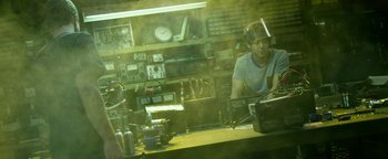 Movie still from “Project Almanac” (2015), directed by Dean Israelite – A man sitting at a table in front of a clock; Medium shot, Over the shoulder angle