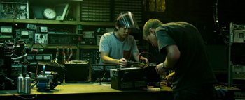 Movie still from “Project Almanac” (2015), directed by Dean Israelite – Two men working on electronics in an electronics shop; Medium shot, Low angle