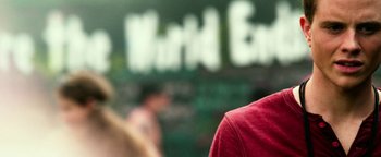 Movie still from “Project Almanac” (2015), directed by Dean Israelite – A man in a red shirt is standing in front of a sign; Close Up shot, Over the shoulder angle