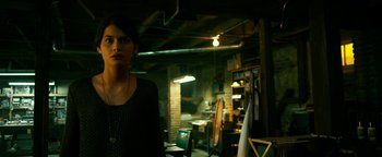 Movie still from “Project Almanac” (2015), directed by Dean Israelite – A woman standing in a room with a lot of furniture; Medium shot, Over the shoulder angle