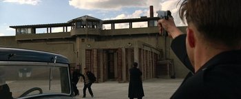 Movie still from “Public Enemies” (2009), directed by Michael Mann – A group of people standing in front of an old building; Wide shot, Over the shoulder angle