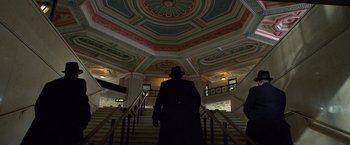 Movie still from “Public Enemies” (2009), directed by Michael Mann – A man in a black coat and hat walking up some stairs; Extreme Wide shot, Low angle