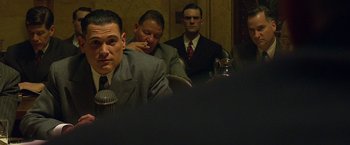 Movie still from “Public Enemies” (2009), directed by Michael Mann – A group of men in suits sitting at a table; Medium shot, Over the shoulder angle