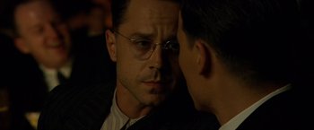 Movie still from “Public Enemies” (2009), directed by Michael Mann – A man in a suit and glasses looking at another man in a suit and glasses; Close Up shot, Over the shoulder angle