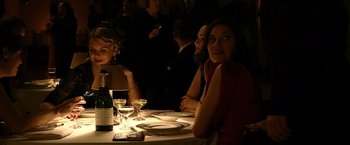 Movie still from “Public Enemies” (2009), directed by Michael Mann – A group of people sitting at a table with wine glasses; Medium shot, Over the shoulder angle