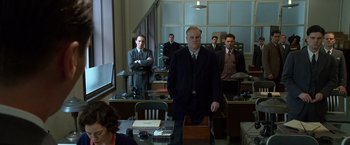 Movie still from “Public Enemies” (2009), directed by Michael Mann – A group of men standing in front of a desk in an office; Medium shot, Low angle