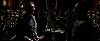 Movie still from “Public Enemies” (2009), directed by Michael Mann – A man standing next to another man in front of a building; Medium shot, Over the shoulder angle