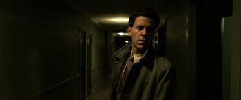 Movie still from “Public Enemies” (2009), directed by Michael Mann – A man standing in a dark hallway wearing a coat and tie; Close Up shot, Low angle