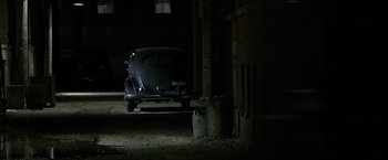 Movie still from “Public Enemies” (2009), directed by Michael Mann – An old car parked in the dark in a garage; Wide shot, High angle