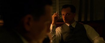 Movie still from “Public Enemies” (2009), directed by Michael Mann – A man sitting in front of a window holding a cell phone up to his ear; Close Up shot, Over the shoulder angle
