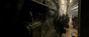 Movie still from “Public Enemies” (2009), directed by Michael Mann – Two men in suits and hats walk by a steam engine train; Wide shot, Low angle