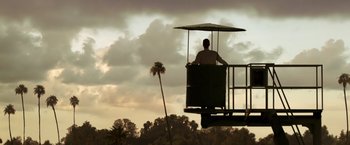 Movie still from “Public Enemies” (2009), directed by Michael Mann – A man standing on top of a platform with an umbrella over his head; Extreme Wide shot, Low angle