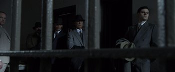 Movie still from “Public Enemies” (2009), directed by Michael Mann – A man in a suit and a hat standing next to another man in a suit and a hat; Medium shot, Low angle
