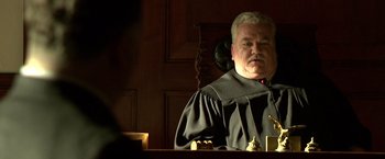 Movie still from “Public Enemies” (2009), directed by Michael Mann – A man in a judge's robe sitting in a courtroom; Close Up shot, Low angle