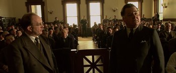 Movie still from “Public Enemies” (2009), directed by Michael Mann – A group of people sitting in front of an audience in a room; Wide shot, High angle