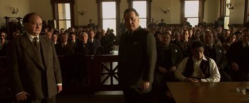 Movie still from “Public Enemies” (2009), directed by Michael Mann – A man standing in front of a group of people in a courtroom; Medium shot, Low angle