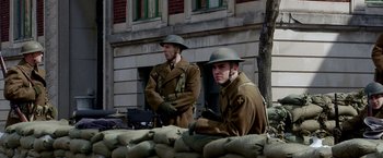 Movie still from “Public Enemies” (2009), directed by Michael Mann – Two men dressed in military uniforms sitting in a sandbag barricade in front of a building; Medium shot, Low angle