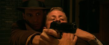 Movie still from “Public Enemies” (2009), directed by Michael Mann – A man holding a gun while another man holds a gun; Close Up shot, Over the shoulder angle