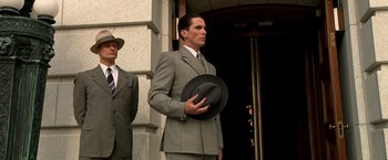 Movie still from “Public Enemies” (2009), directed by Michael Mann – A man in a suit and tie holding a hat; Medium shot, Low angle