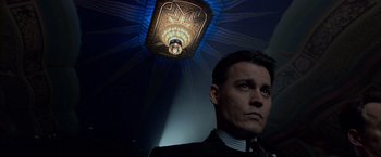 Movie still from “Public Enemies” (2009), directed by Michael Mann – A man in a suit and tie in front of a light fixture; Close Up shot, Low angle