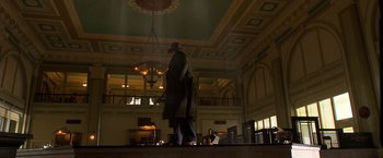 Movie still from “Public Enemies” (2009), directed by Michael Mann – A man in a long coat and hat walking in a room; Wide shot, Low angle