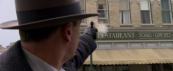 Movie still from “Public Enemies” (2009), directed by Michael Mann – A man holding a gun pointed at a restaurant sign; Medium shot, Low angle