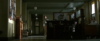 Movie still from “Public Enemies” (2009), directed by Michael Mann – A man standing in a dark room in front of a desk; Wide shot, Low angle