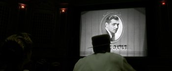 Movie still from “Public Enemies” (2009), directed by Michael Mann – A man wearing a hat looking at an image on a screen; Close Up shot, Low angle
