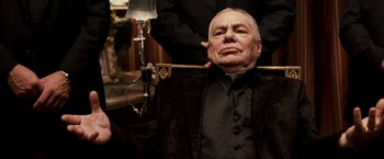 Movie still from “Punisher: War Zone” (2008), directed by Lexi Alexander – An older man is sitting in a chair; Medium shot, Low angle