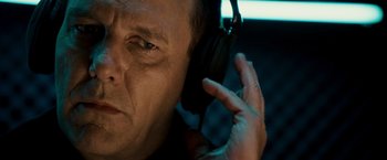 Movie still from “Punisher: War Zone” (2008), directed by Lexi Alexander – A person wearing headphones with one hand up to his ear; Close Up shot, Overhead angle
