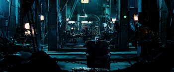 Movie still from “Punisher: War Zone” (2008), directed by Lexi Alexander – A man sitting in a chair in front of a machine shop; Wide shot, High angle