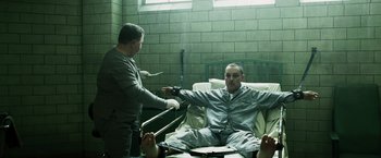 Movie still from “Punisher: War Zone” (2008), directed by Lexi Alexander – A man sitting on a hospital bed while another man holds a gun; Medium shot, High angle