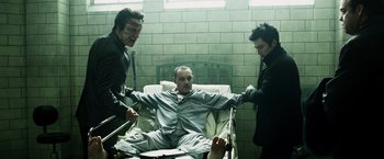 Movie still from “Punisher: War Zone” (2008), directed by Lexi Alexander – A man in a hospital bed being assisted by two other men; Medium shot, High angle