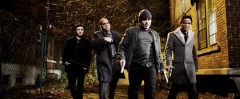 Movie still from “Punisher: War Zone” (2008), directed by Lexi Alexander – A group of men standing next to each other on a field; Medium shot, Low angle