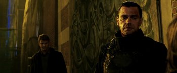 Movie still from “Punisher: War Zone” (2008), directed by Lexi Alexander – A man standing next to another man in front of a wall; Close Up shot, Over the shoulder angle
