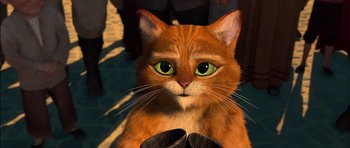 Movie still from “Puss in Boots” (2011), directed by Chris Miller – An orange cat with green eyes sitting next to a person; Close Up shot, High angle
